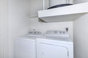 A white washing machine and dryer in a small laundry room.at Century Cedar Hill, Cedar Hill, 75104
